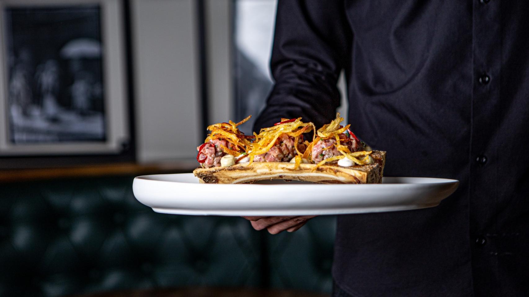 Un camarero sostiene un plato en su camino hacia una mesa, en imagen de archivo.
