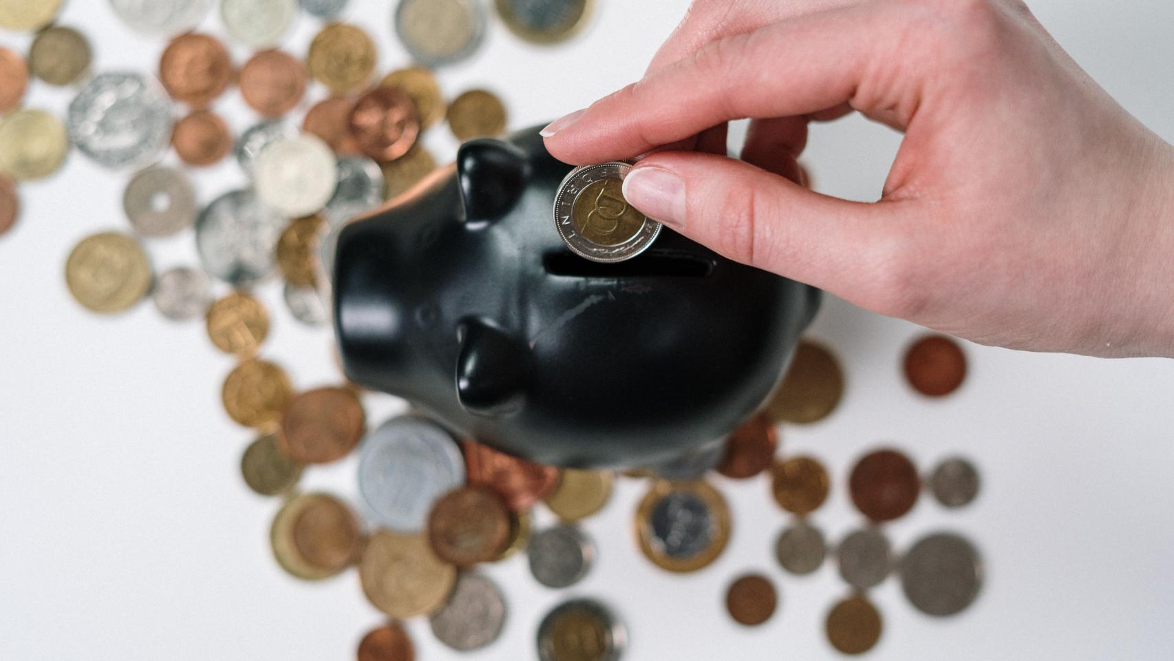 Una persona introduce una moneda en una hucha.