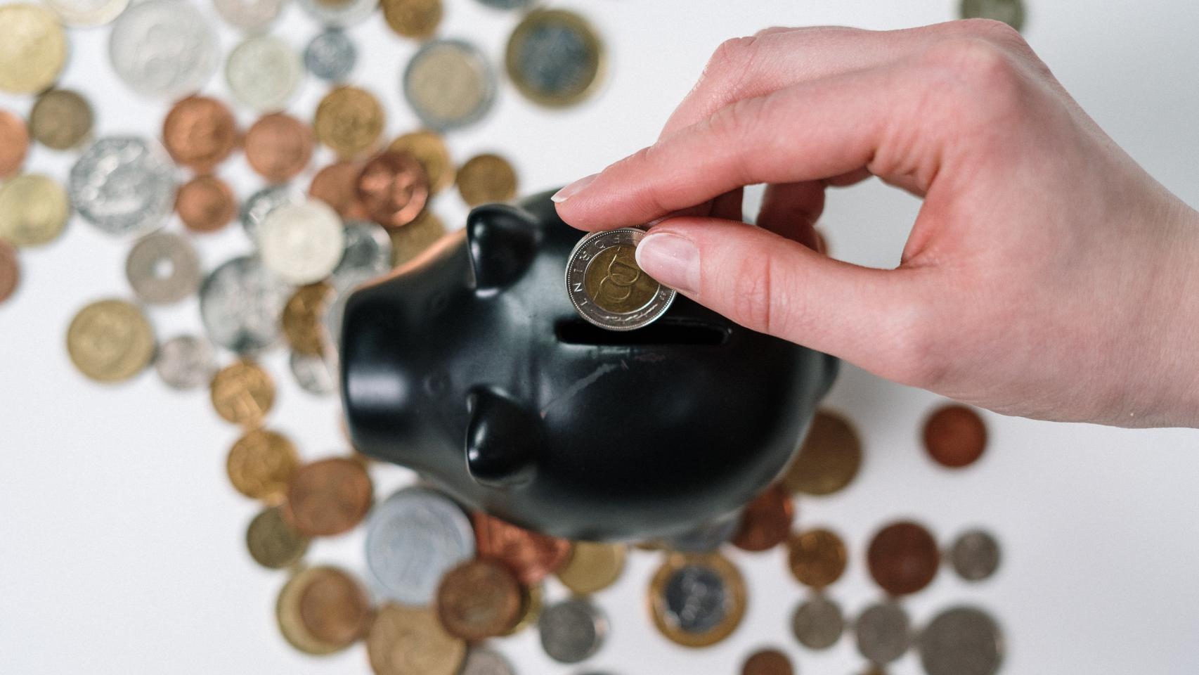 Una persona introduce una moneda en una hucha.