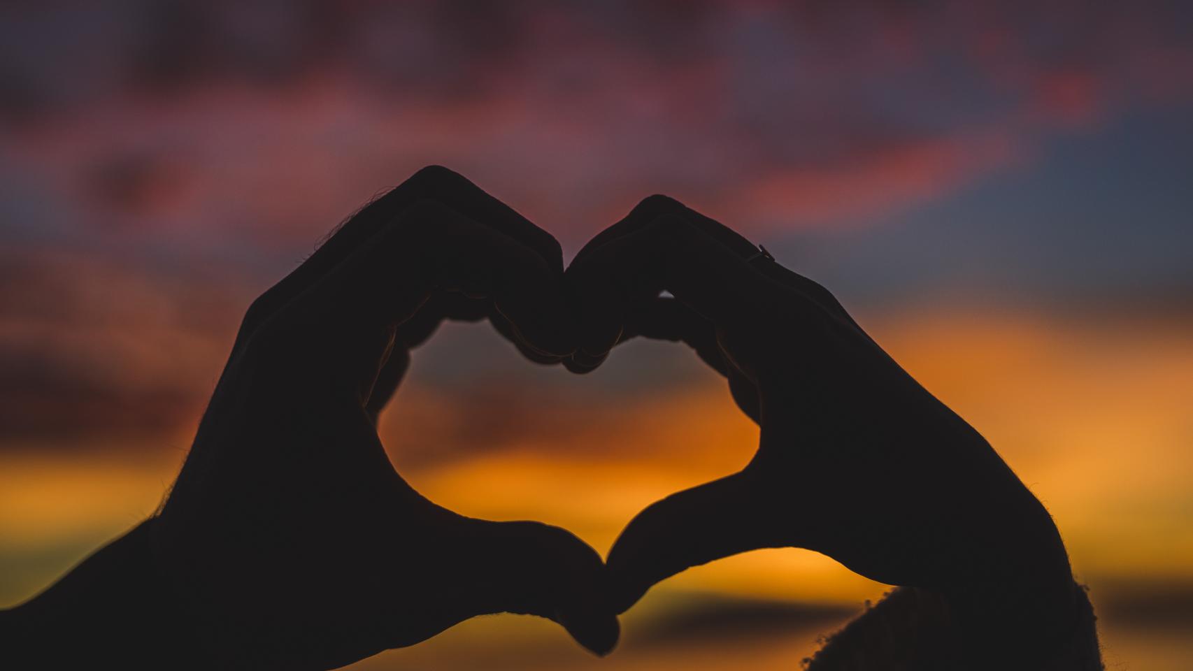 Pareja haciendo forma de corazón con los dedos.
