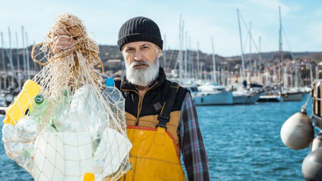 Un pescador sostiene una red llena de plásticos.