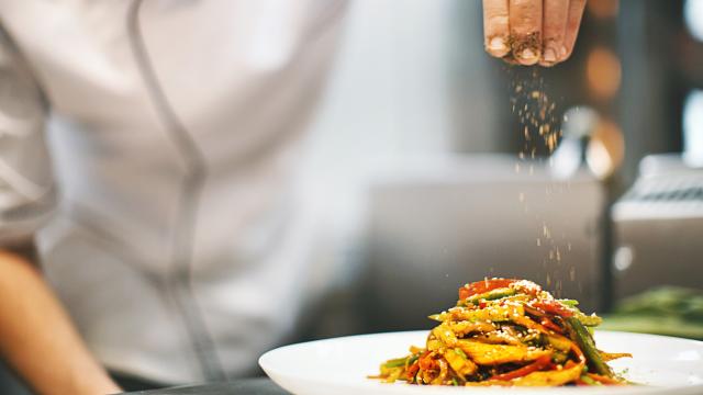 Un cocinero echándole semillas a un plato de verdura.