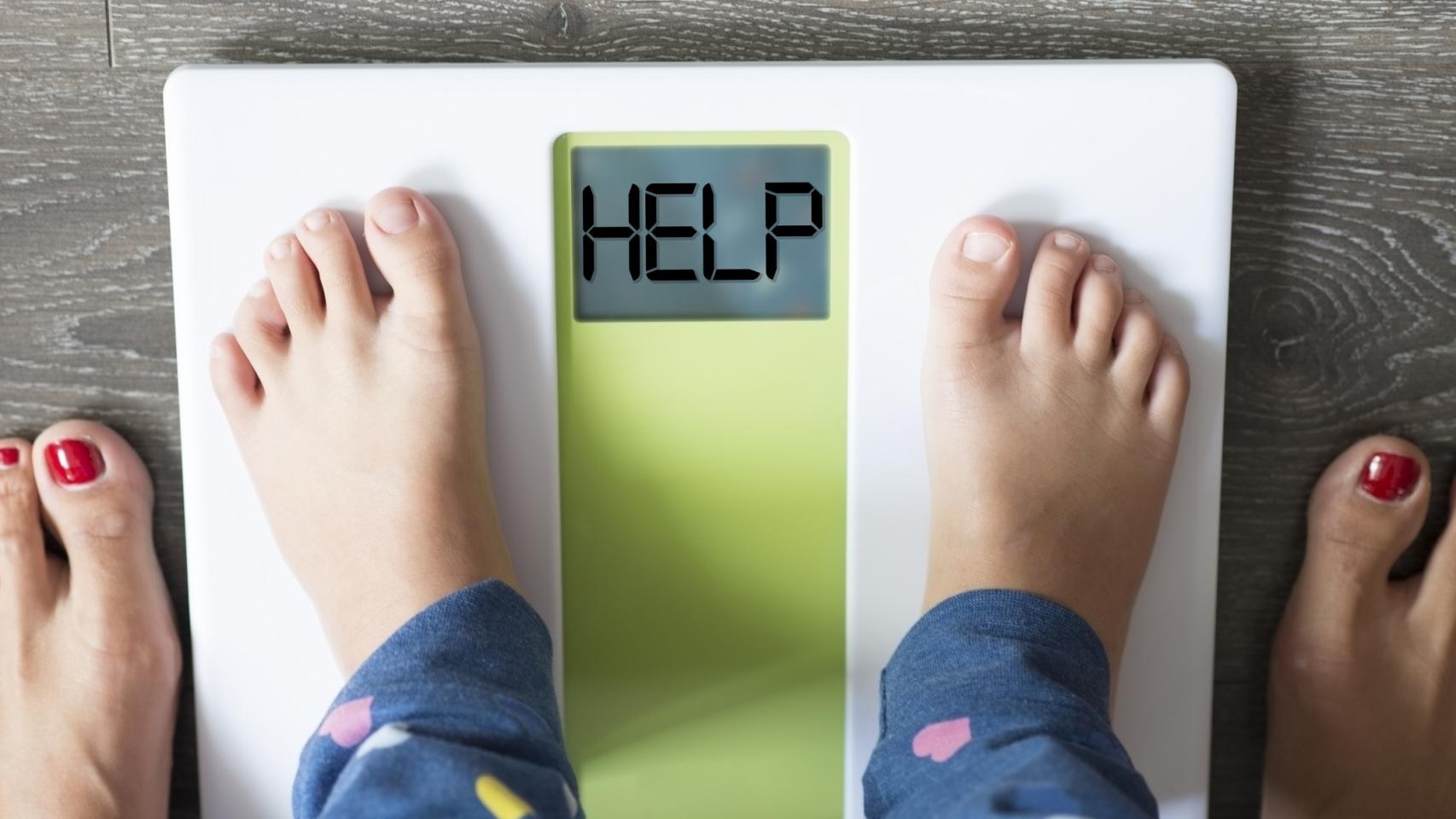 Los pies de un niño sobre una báscula que indica 'AYUDA'.