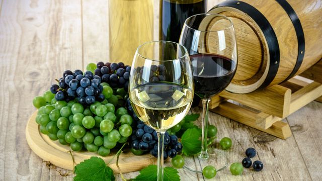 Una copa de blanco y otra de tinto junto auna barrica.