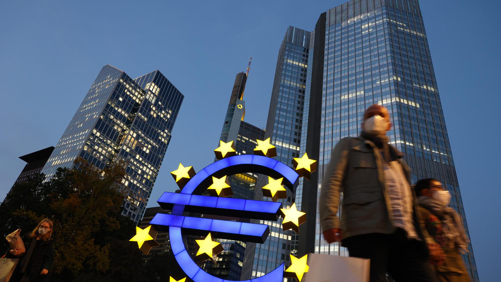 La sede del Banco Central Europeo iluminada de noche mientras dos turistas pasean por delante.