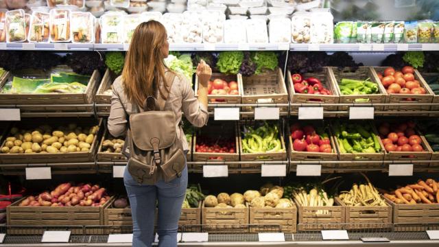 Una mujer frente a un estante de verduras y hortalizas.