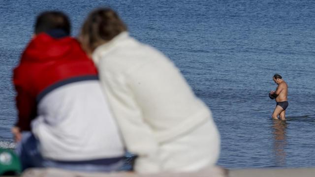 Dos personas contemplan a un bañista en una playa valenciana a principios de semana.