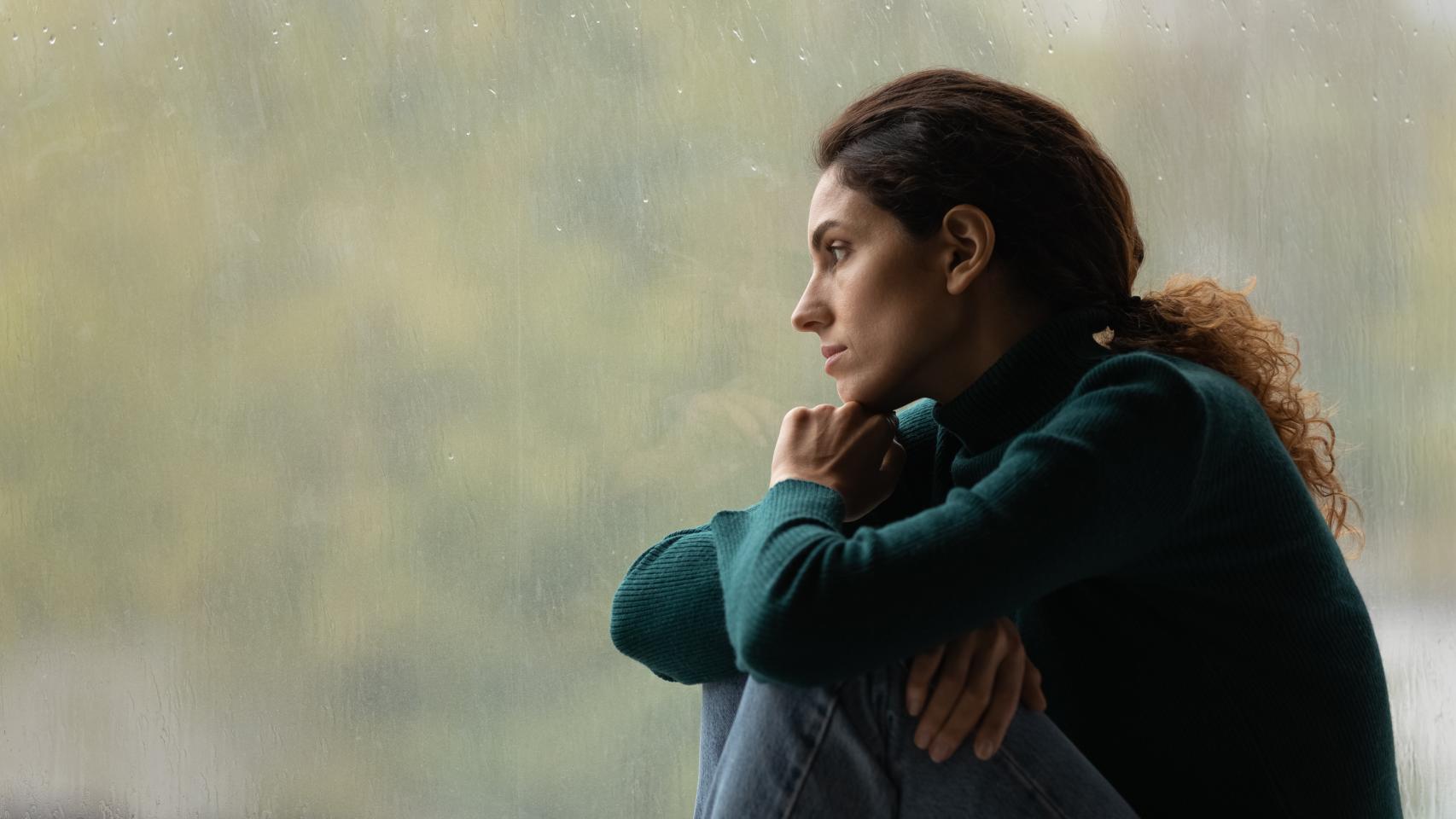 Una mujer triste mira por la ventana.