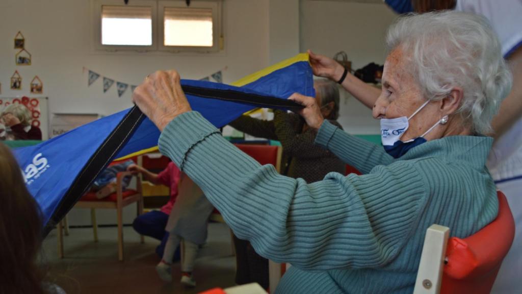 Una anciana juega al 'paracaídas' este viernes con los niños de la escuela infantil.