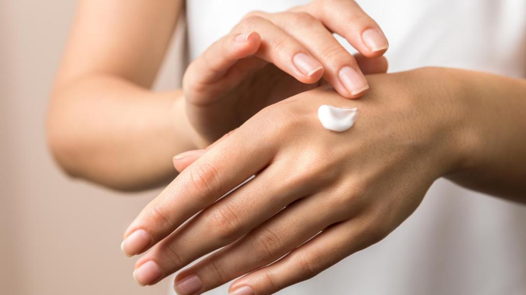 Unas manos de mujer joven aplicando crema hidratante.