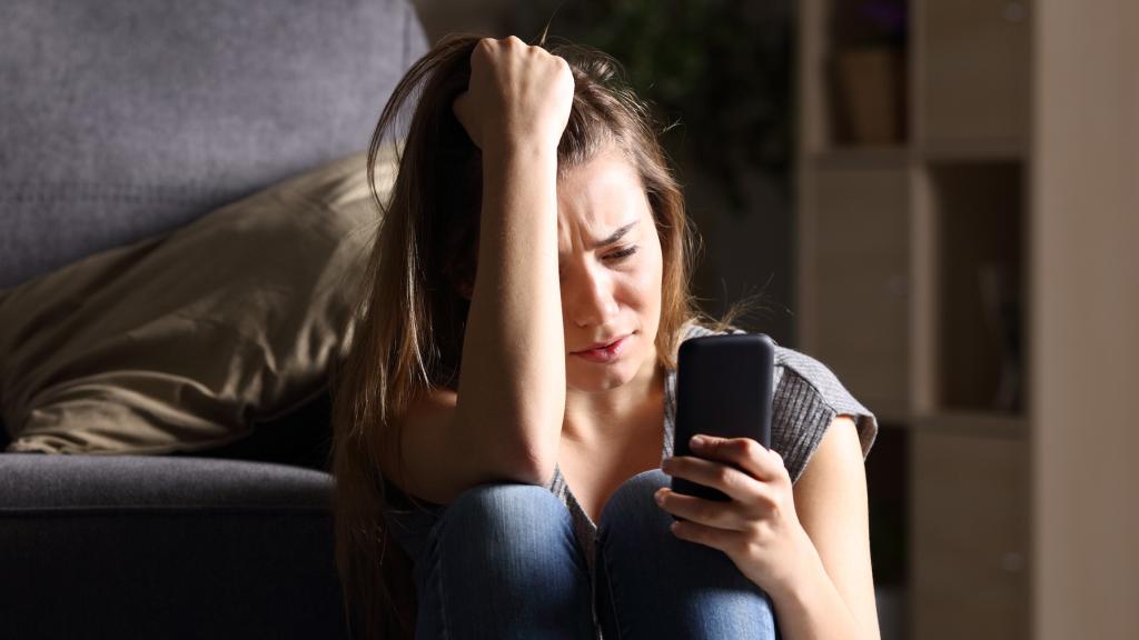 Una joven mira su teléfono llorando.