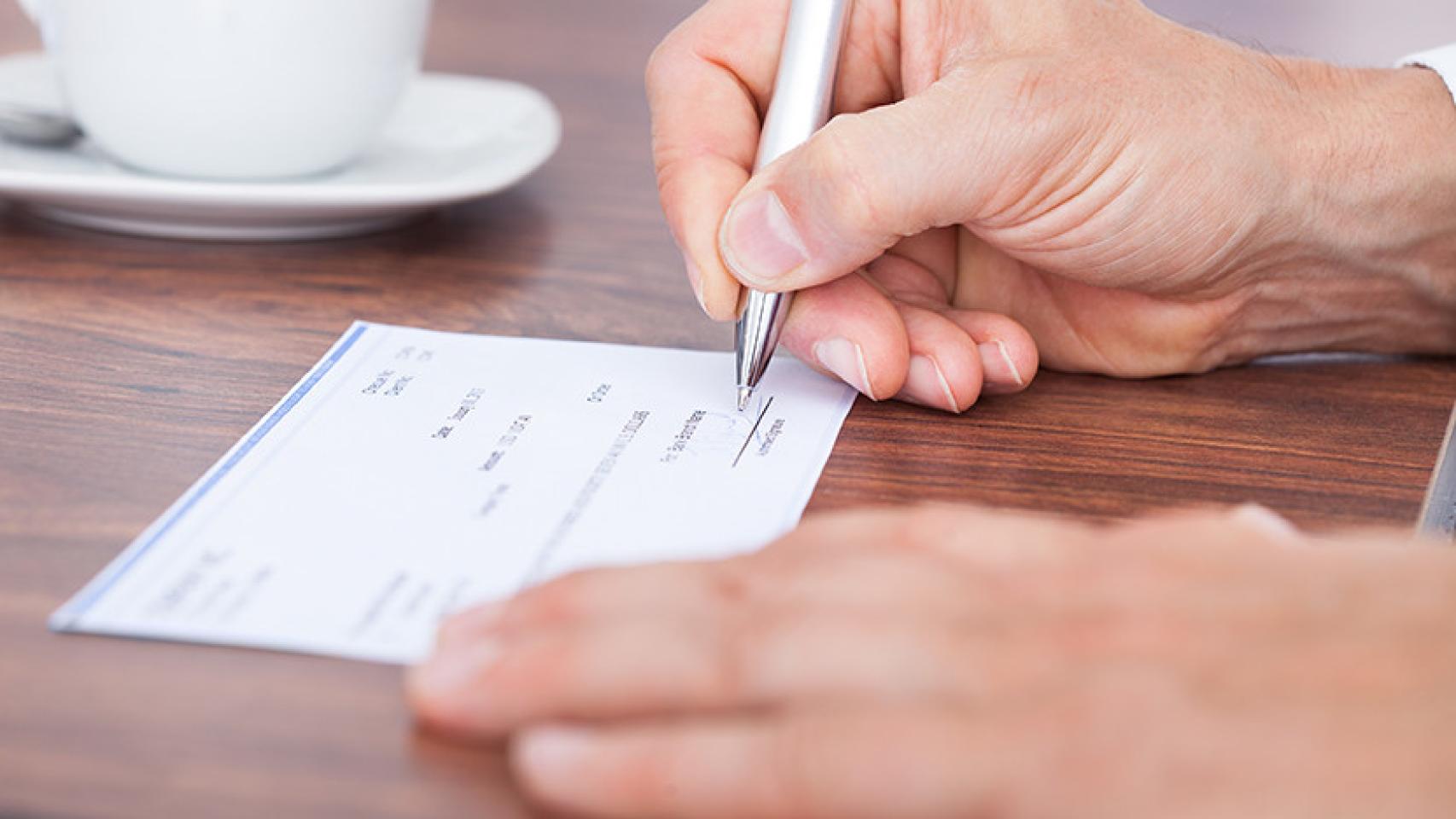 Un hombre rellenando un cheque, en imagen de archivo.