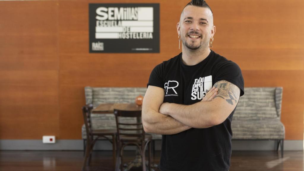 Carlos Maldonado, sonriendo y con el cartel de fondo de la escuela Semillas.