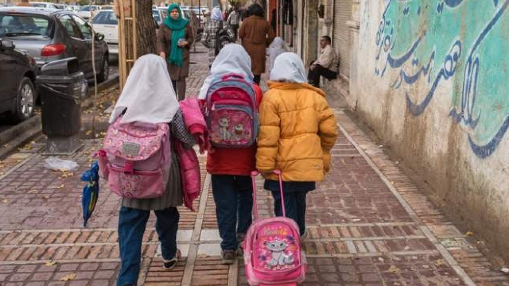 Tres niñas iraníes pasean con sus mochilas por una calle de Teherán.