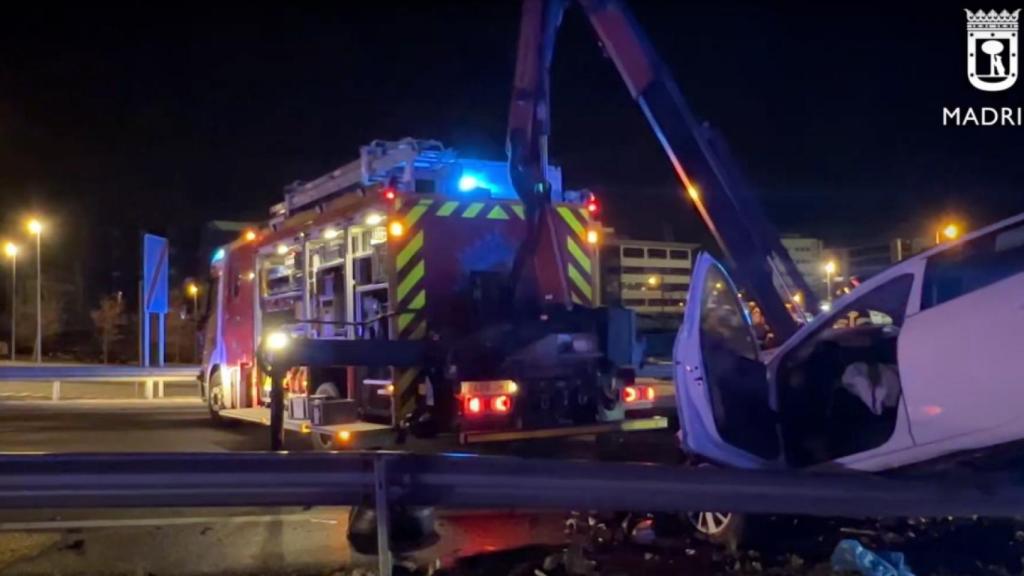 Los bomberos retiran el malogrado taxi, que terminó subido a un guardarraíl por el impacto.