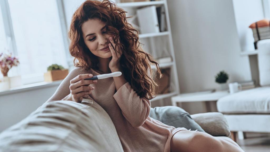 Una mujer sonríe con un test de embarazo positivo.