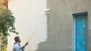 Un hombre pintando con rodillo el muro exterior de una casa