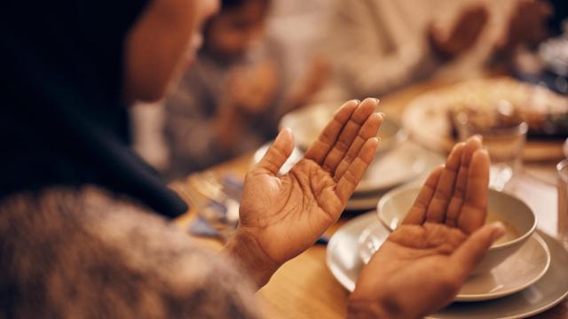 Una mujer musulmana reza con su familia en la mesa del comedor.