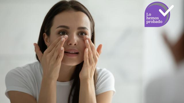 Una mujer se aplica un tratamiento de contorno de ojos ante el espejo.