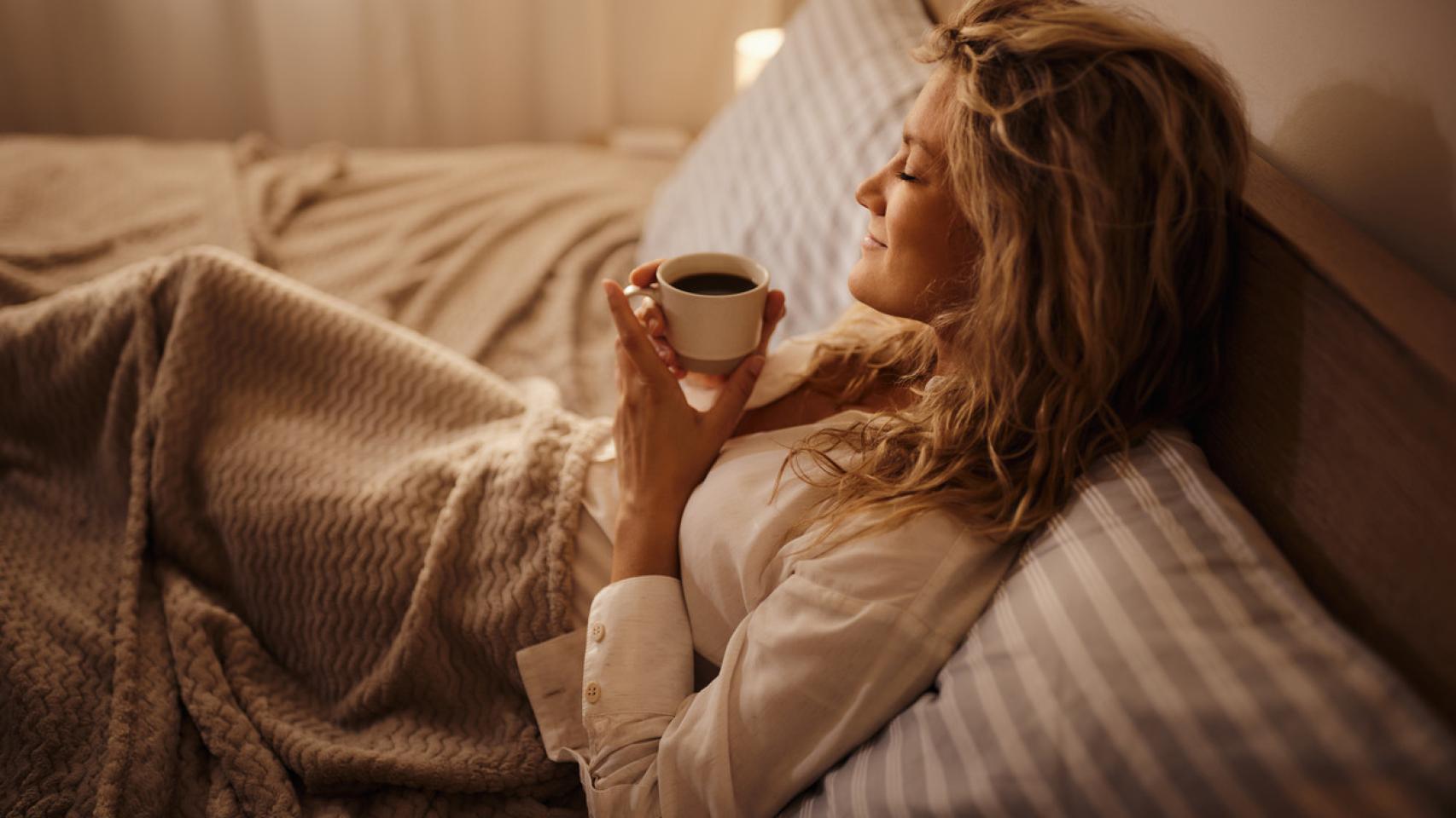 Mujer relajada disfrutando de una bebida en la cama.