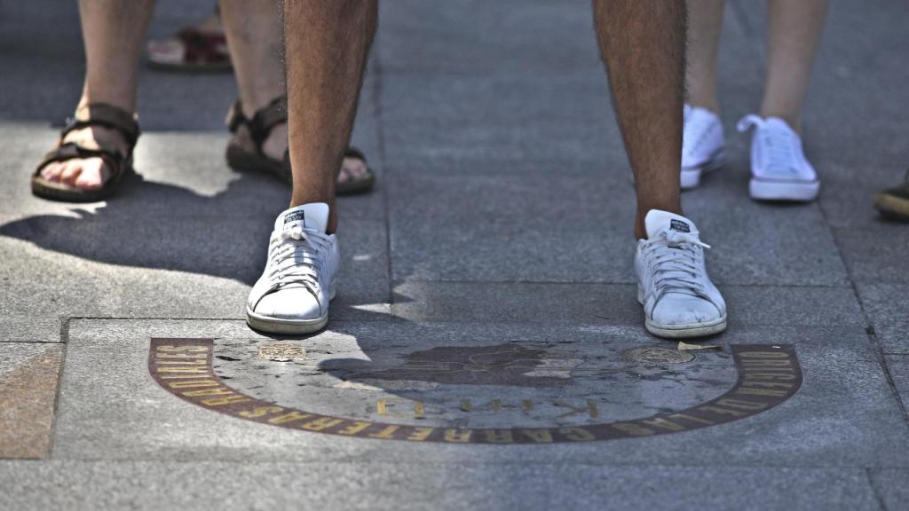 Unos viandantes se paran en la antigua placa del Kilómetro Cero en  la Puerta del Sol.