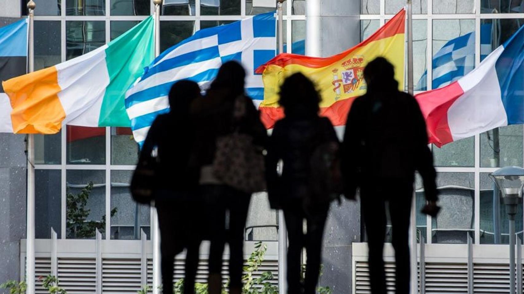 Varios jóvenes caminan entre banderas de países miembros de la Unión Europea, en Bruselas.