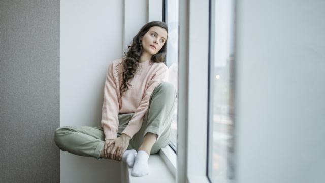 Una joven mira triste por la ventana.