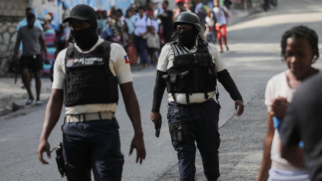 Oficiales de policía caminan cerca de personas que cargan sus pertenencias mientras huyen de sus hogares.