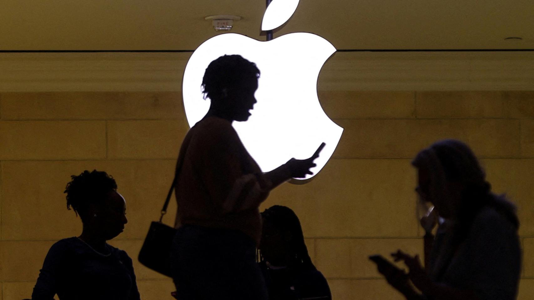 Una mujer usando su iPhone frente al letrero luminoso de la tienda de Apple en la estación Grand Central de Nueva York.