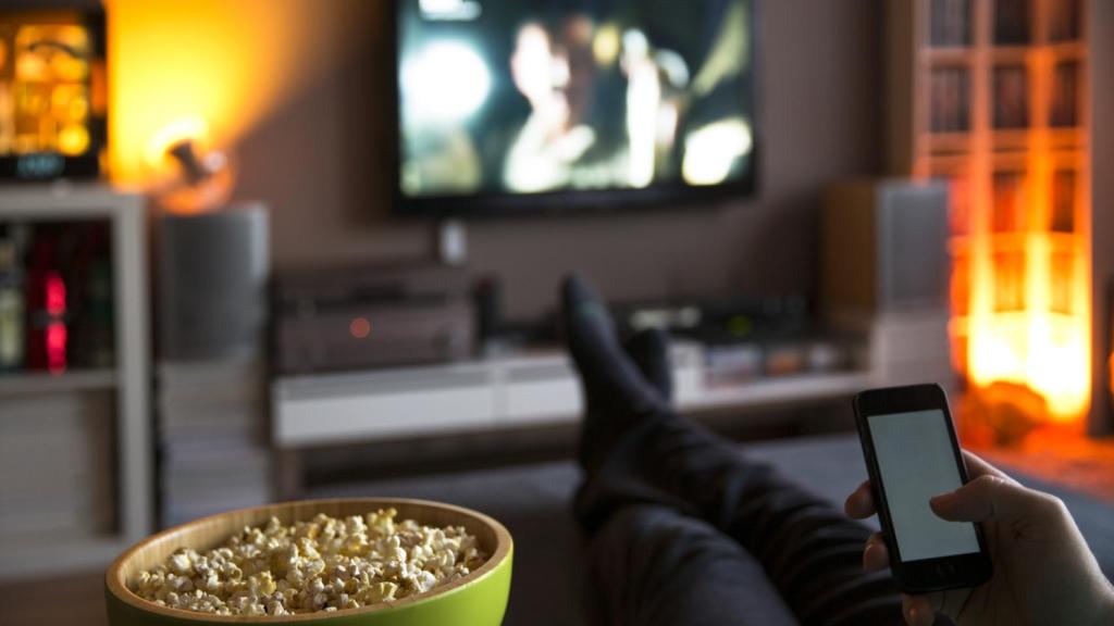 Un hombre mira su móvil y la televisión al mismo tiempo.