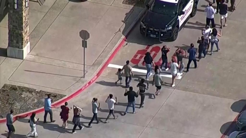 Un grupo de personas, con las manos en alto, abandona el centro comercial de Allen.
