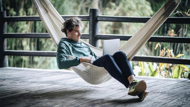 Un joven teletrabajando en una hamaca.