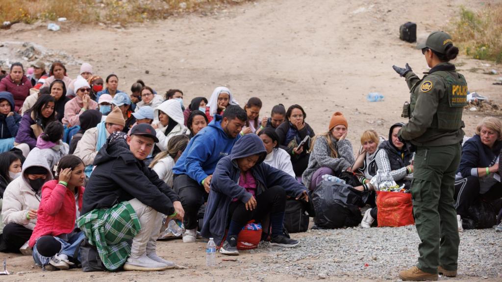 Una agente fronteriza estadounidense habla con migrantes entre la primera y la segunda valla fronteriza, este miércoles.