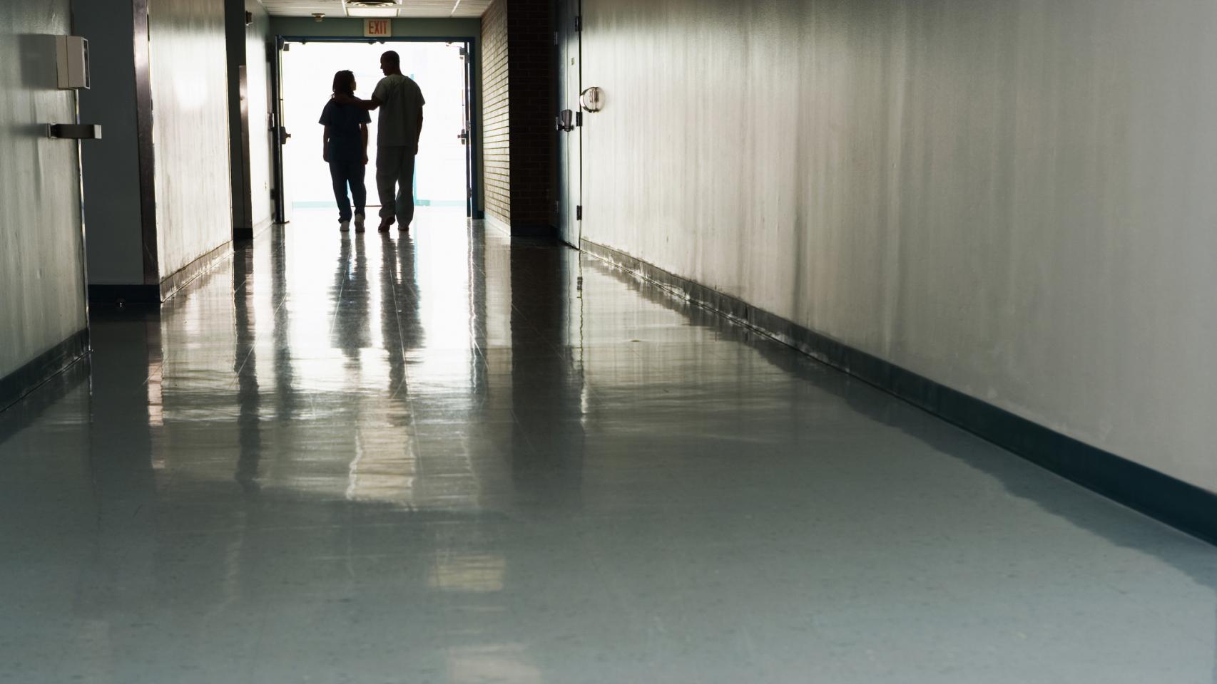 Dos personas caminan por un pasillo de hospital.