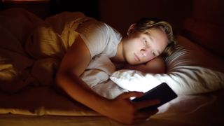 Imagen de archivo de un adolescente utilizando el móvil por la noche en una cama.