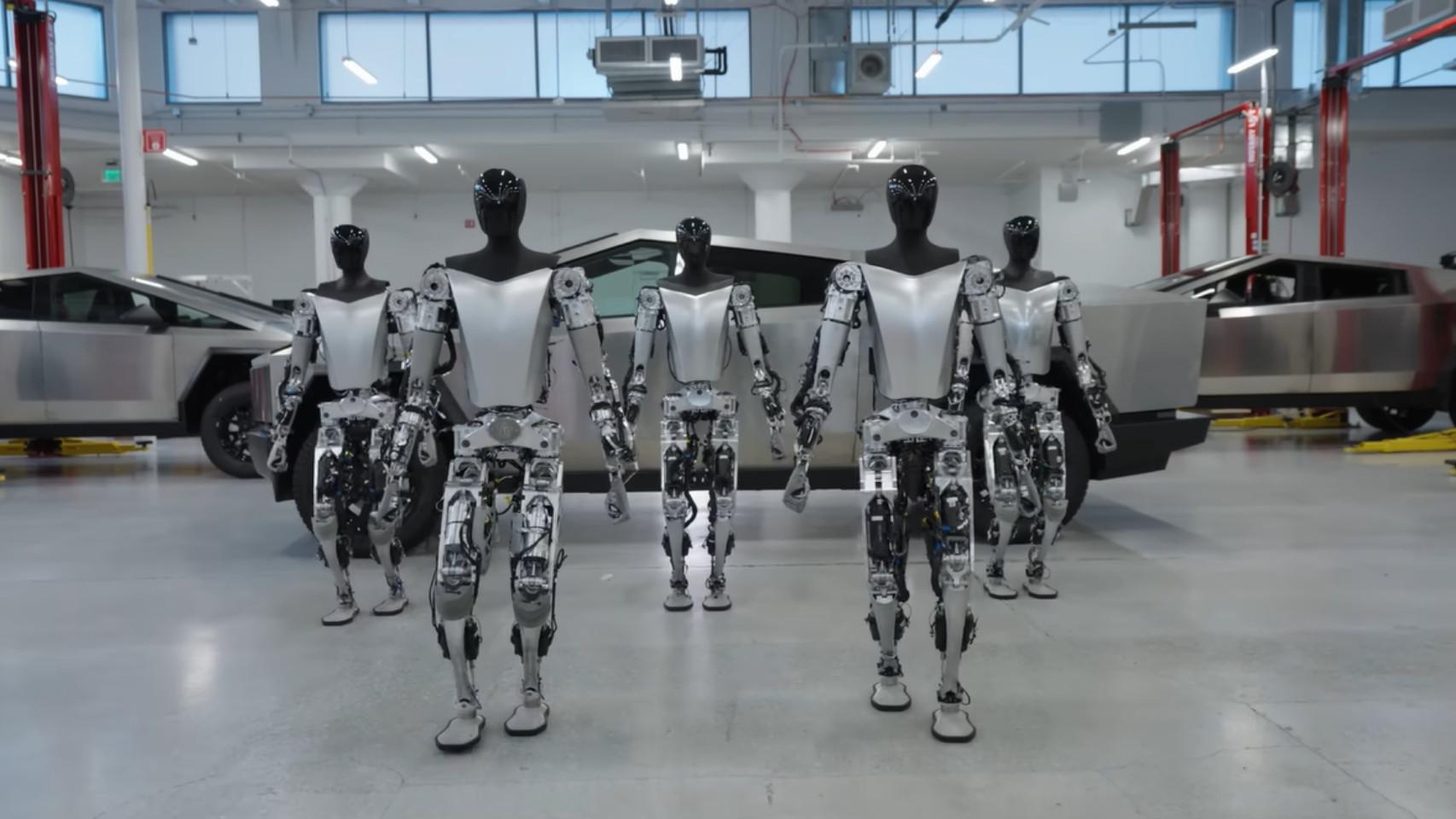 Varios robots humanoides de Tesla caminando con algunos Cybertruck de fondo.