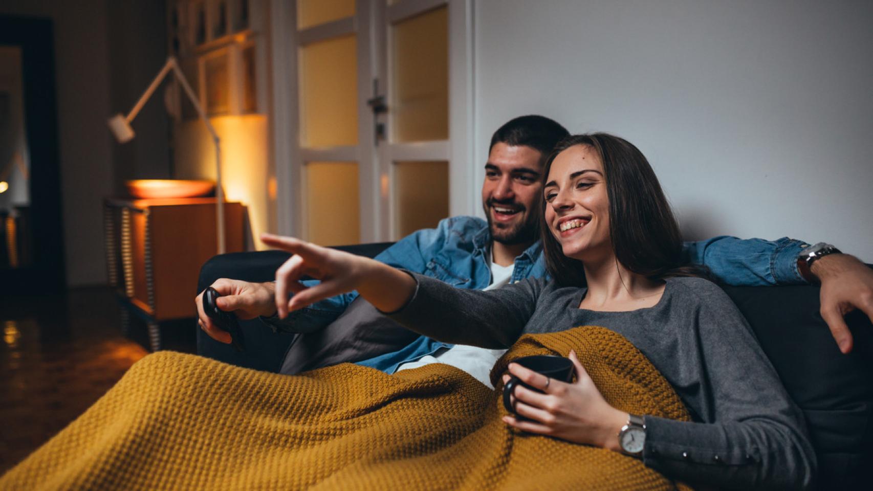 Una pareja en el sofá y con manta viendo la tele.