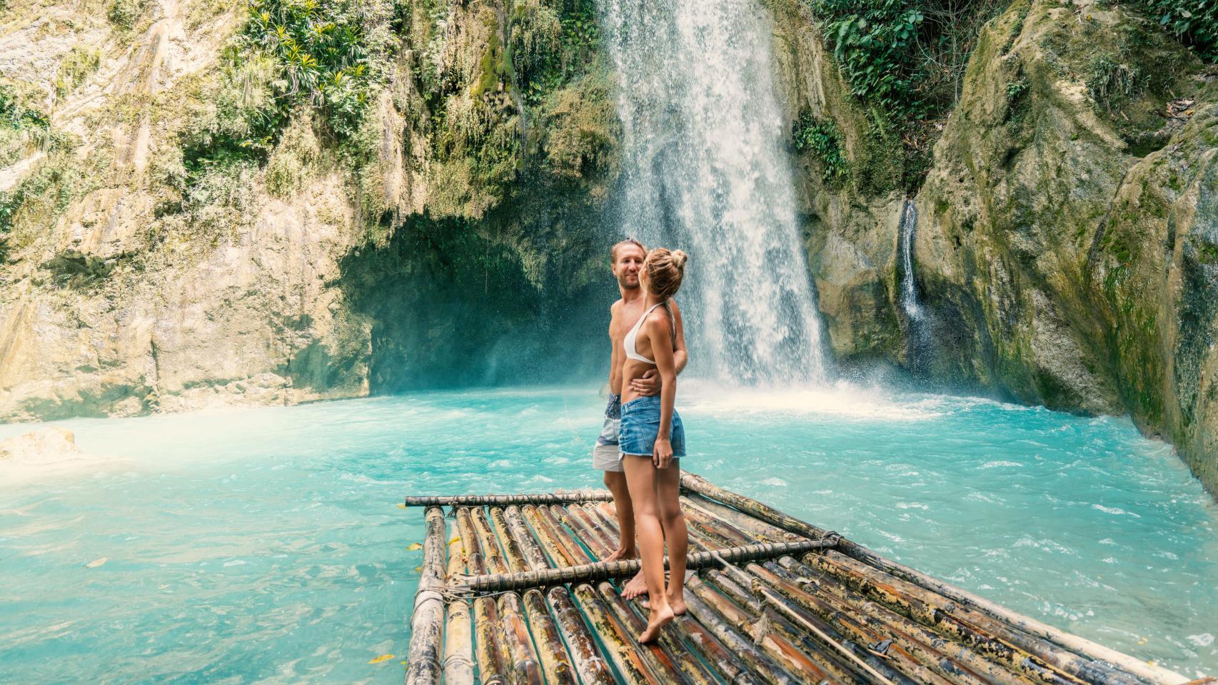 Pareja joven disfruta de una excursión frente a una cascada.