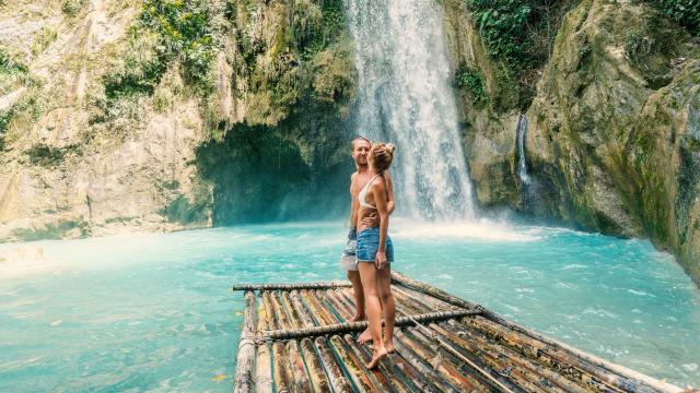 Pareja joven disfruta de una excursión frente a una cascada.