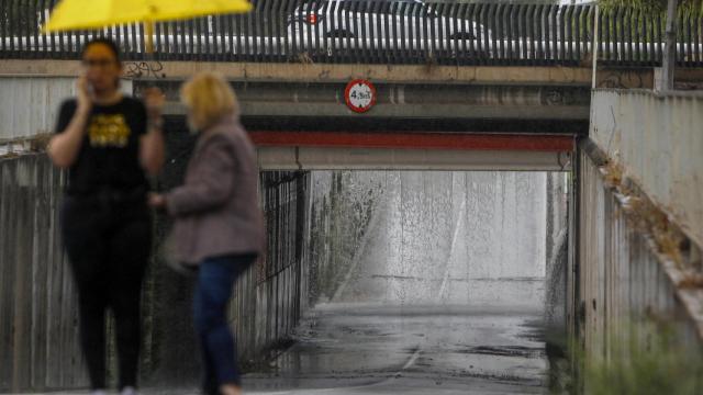 Dos personas aguardan ante el paso inferior a la entrada de San Vicente desde la carretera de La Alcoraya cortada por las intensas lluvias.