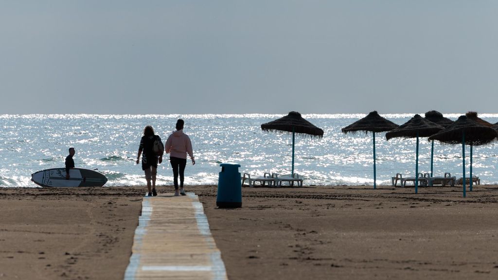 Dos personas caminan por una pasarela de madera en una playa valenciana, hace unas semanas.