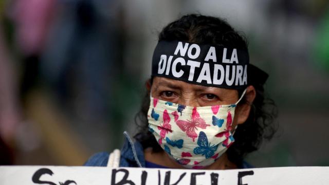 Una manifestante lleva una cinta con el mensaje No a la dictadura y soporta una pancarta contra Bukele.
