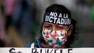 Una manifestante lleva una cinta con el mensaje No a la dictadura y soporta una pancarta contra Bukele.