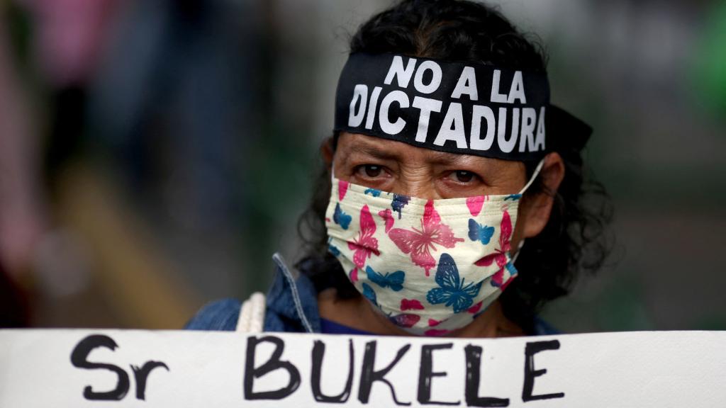 Una manifestante lleva una cinta con el mensaje No a la dictadura y soporta una pancarta contra Bukele.