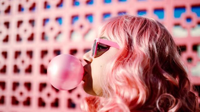 Imagen de archivo de una persona con el pelo rosa haciendo una pompa con un chicle.