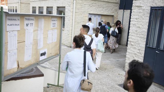 Varias personas miran los carteles con indicaciones para realizar las pruebas para docentes.