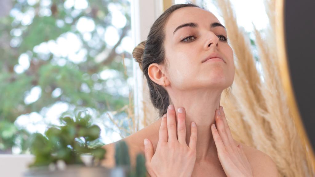 Mujer mirando su cuello ante el espejo.