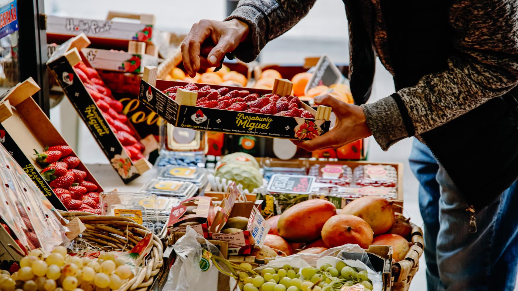 Una persona coge una caja de fresas en una frutería.