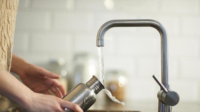 Persona llenando una botella de agua del grifo.