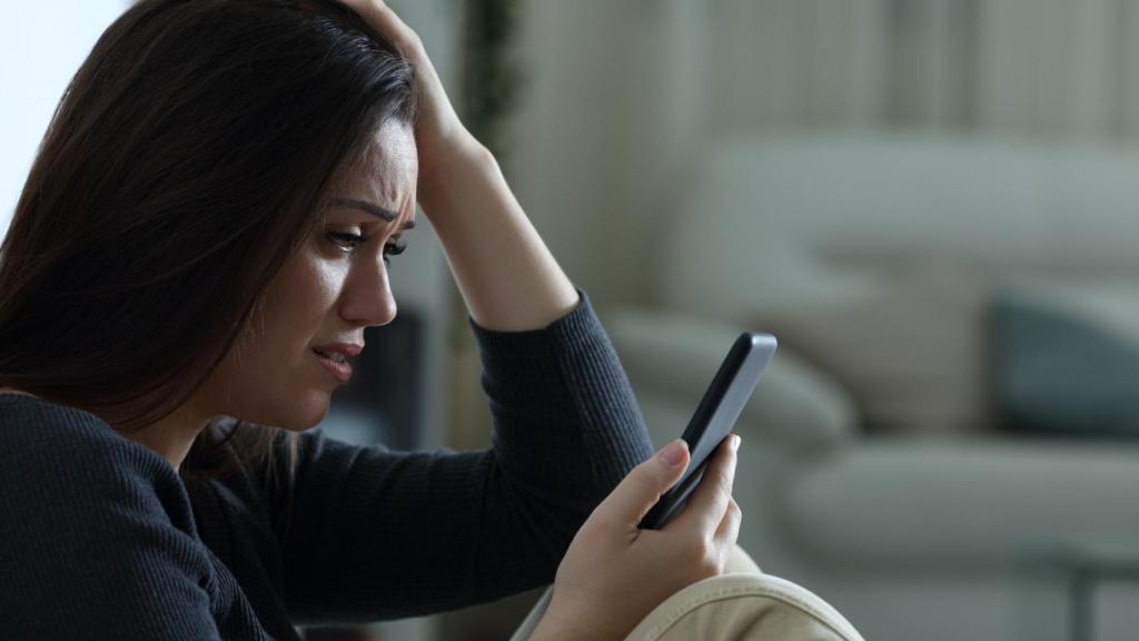 Una mujer triste y asustada mirando su teléfono.